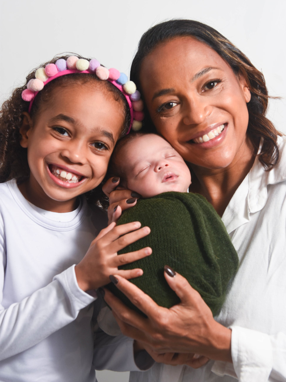 Mãe e filha sorrindo abraçadas ao bebê recém-nascido enrolado em manta verde