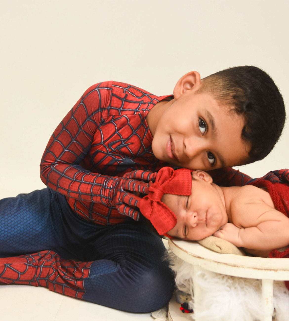 Menino com fantasia de Homem-Aranha deitado ao lado da irmã recém-nascida