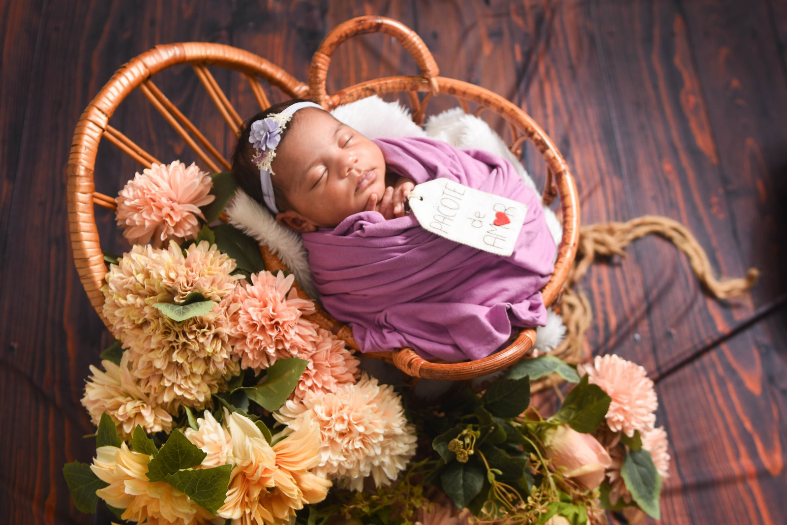 Recém-nascida em cesto de vime com manta lilás e flores
