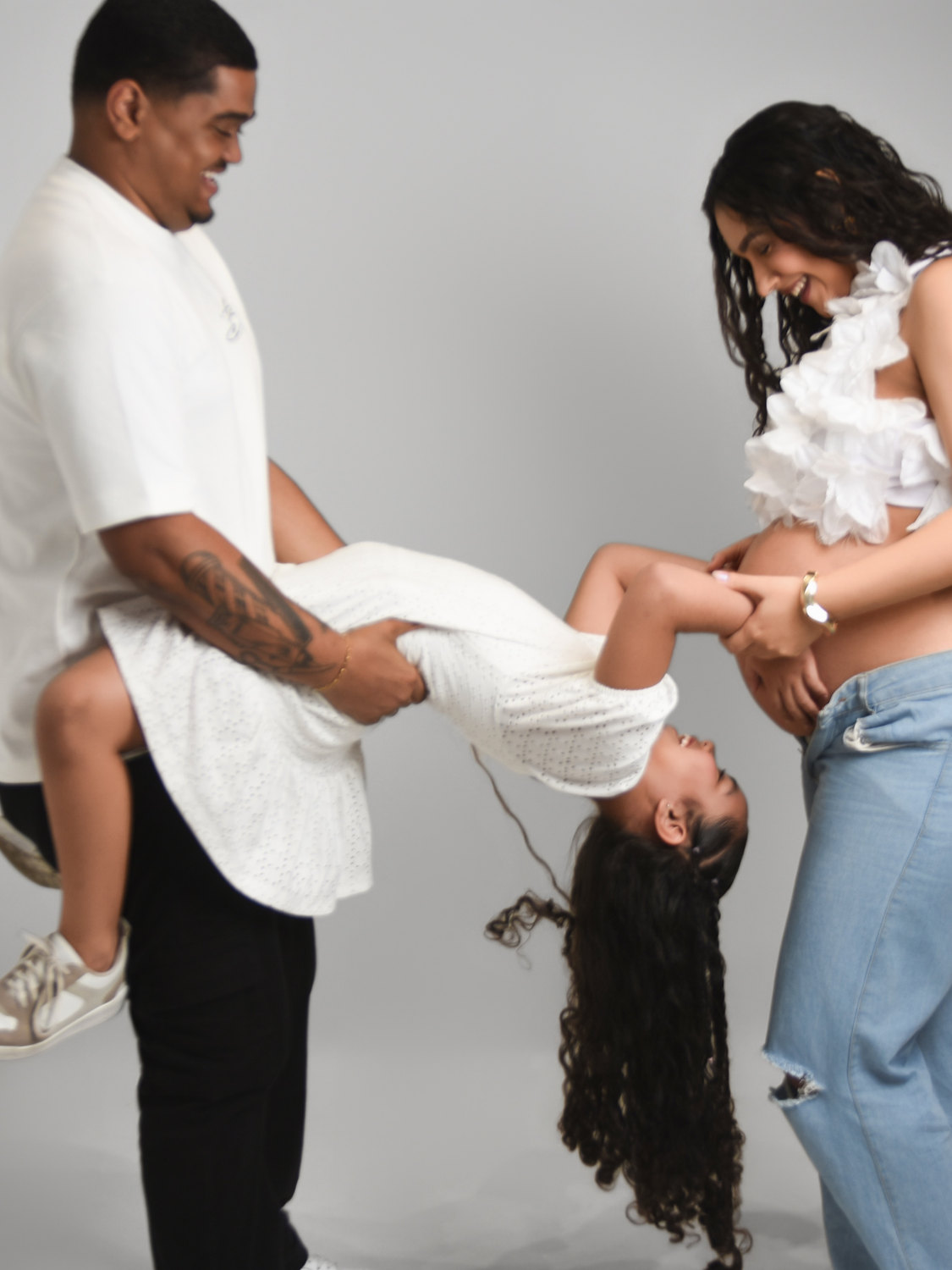 Pai brincando de virar a filha de cabeça pra baixo ao lado da mãe grávida