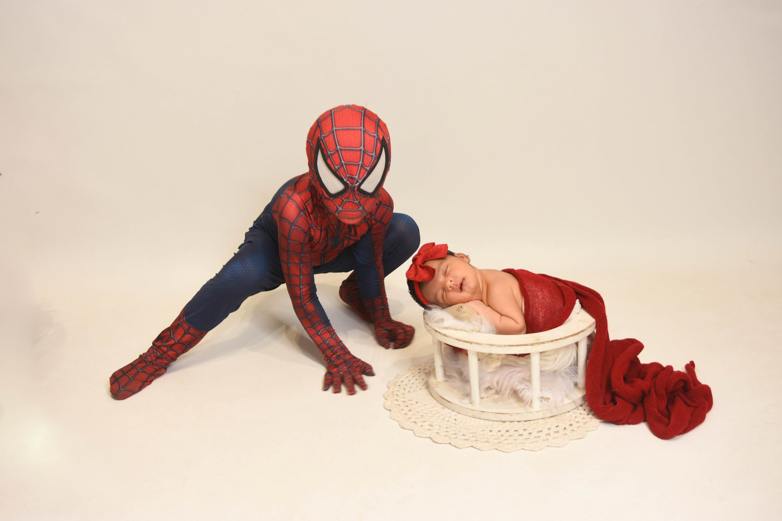 Irmão fantasiado de Homem-Aranha agachado ao lado da irmã recém-nascida